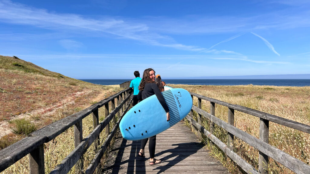 Alumnos yendo a surfear por el paseo de madera de la playa de Mar de Fora