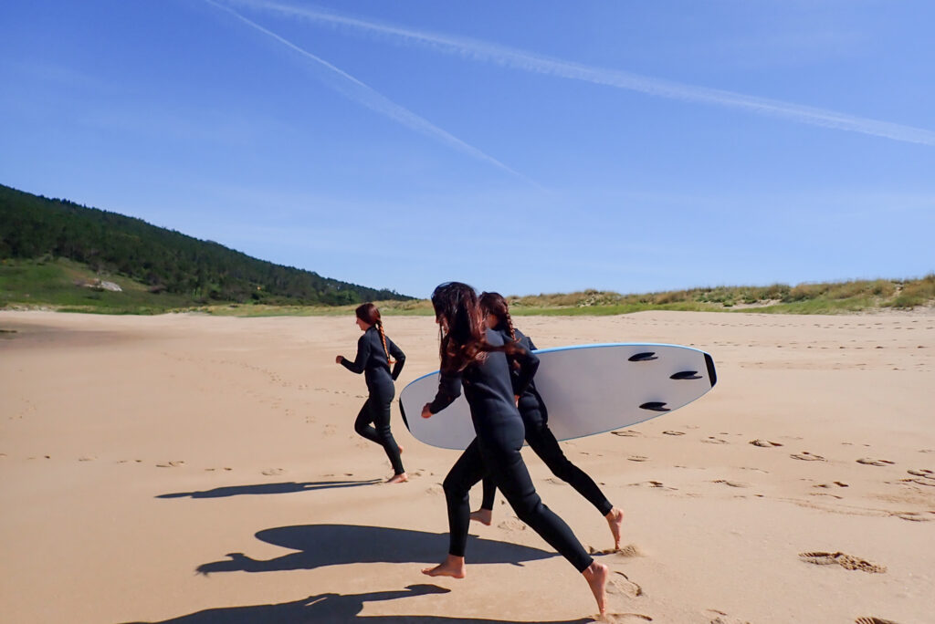 Alumnas de la Eric Rebière Surf Academy corriendo por la playa para ir a surfear en las olas de Mar de Fora
